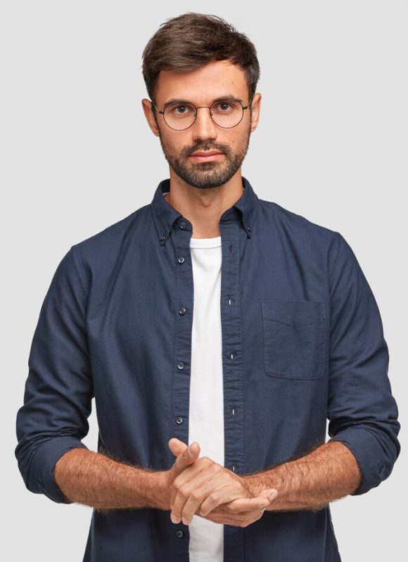 waist-up-portrait-handsome-serious-unshaven-male-keeps-hands-together-dressed-dark-blue-shirt-has-talk-with-interlocutor-stands-against-white-wall-self-confident-man-freelancer_273609-16320